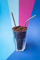 Fototapeta na wymiar The glass with coffee beans and two reusable steel straws on the blue and pink background. Plastic free concept.