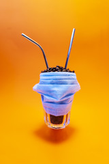 Glass with coffee beans and two reusable steel straws, floating in the air. Medical mask. Creative bright orange background. Pandemic and plastic free concept. Minimal concept idea. Copy space.