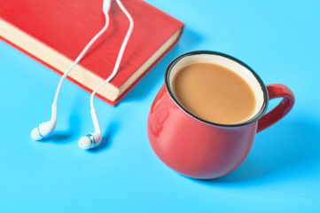Headphone and old book near red cup full of coffee on blue background. Audiobook concept. Online education. E-learning. Modern technology