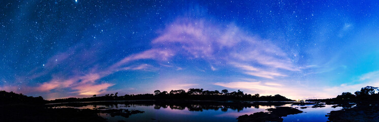 Panorama of a river at night with part of milky way and colorful clouds