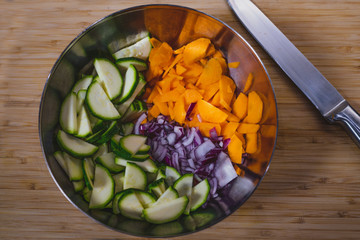 bowl of onions, courgettes and carrots cut into cubes on a bamboo cutting board with the steel...