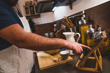 boy prepares a pizza dough following a recipe on the tablet in his home kitchen during the lockdown for covid 19