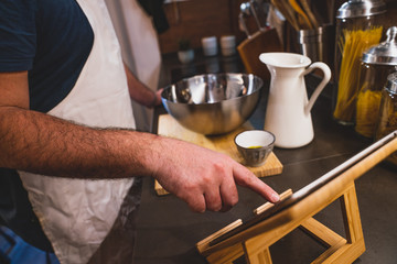 boy prepares a pizza dough following a recipe on the tablet in his home kitchen during the lockdown for covid 19