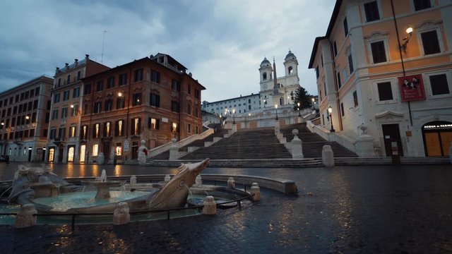Fountain at Piazza di Spagna, the Spanish Steps stairway in the background, dark, rainy evening, in Rome - tracking tilt up shot