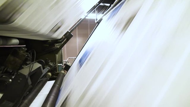 Newspaper pages moving on a printing machine belt line, inside a print facility - Dolly view
