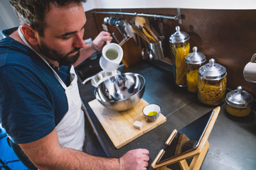 boy prepares a pizza dough following a recipe on the tablet in his home kitchen during the lockdown for covid 19
