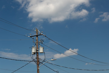 Power pole and lines with transformers and street light, blue sky with clouds, horizontal aspect