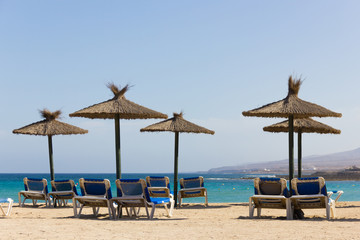 Wicker sun umbrellas with blue hammocks on empty beach in Fuerteventura. Nobody on sunny day in Caleta de Fuste, Canary Islands. Summer holidays, tourism crisis concepts
