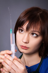 A young nurse uses a syringe with medicine. Girl, brunette on a gray background.