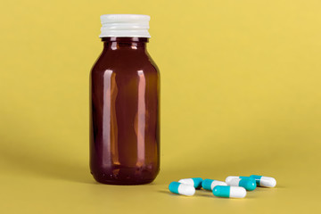 Big medicine glass bottle with blue medicines, cap on and yellow background