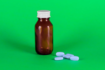 Big medicine glass bottle with blue medicines, cap on and green background