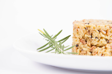 Risotto with button mushroom and bacon decorated with rosemary twig on a plate on a white background
