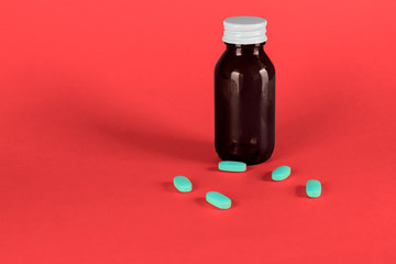 Big medicine glass bottle with blue capsules, cap off and red background