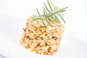 Risotto with button mushroom and bacon decorated with rosemary twig on a plate on a white background