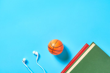 White headphone and old books, toy basketball ball on blue background. Audiobook concept. Online education. E-learning. Modern technology