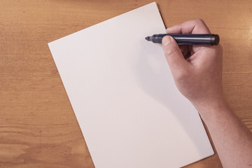 Man's hand writing on a paper on a wooden table. preparation of report or notice.