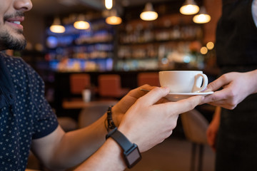 Happy young man taking cup of tea or coffee from hands of waitress