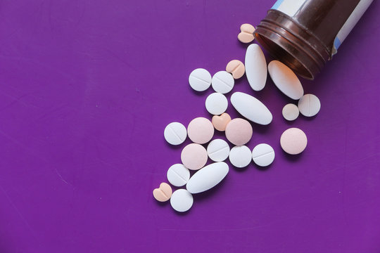 pills spilling from a container on purple background 