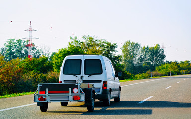 Fototapeta na wymiar Mini van carrying trailer in asphalt road in Slovenia reflex