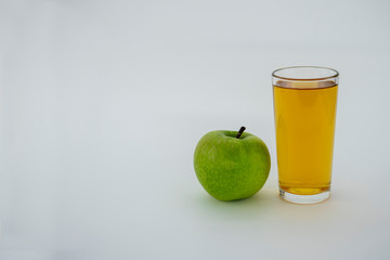 a glass of Apple juice next to an Apple on a white background