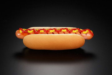 Classic hot dog with ketchup and mustard on a black background.