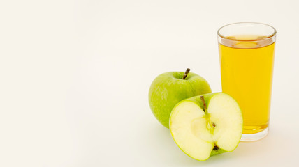 a glass of Apple juice next to an Apple on a white background