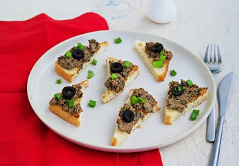 Chicken liver appetizer with salted olives on slices of toasted white bread on a light concrete plate. Offal recipes. Appetizer Recipes. Italian food.