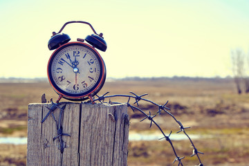 Old retro alarm clock on post tied with barbed wire symbolizes arrival of spring.