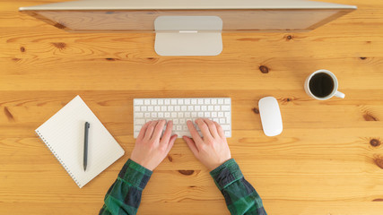 Image from above of man drinking coffee and writing at notebook during the day.