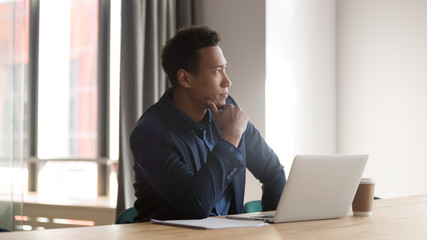 Mixed race entrepreneur sit at desk in front of laptop looking out the window, african businessman...