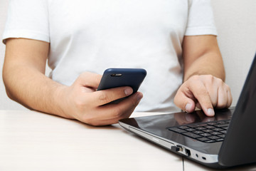 Close-up: a man holding a phone and working at a computer in the office