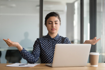 Calm office worker hindu woman sit at desk near laptop folded fingers mudra gesture take break...