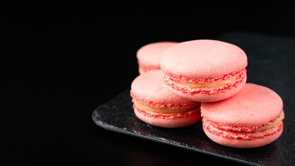 pink macaroons on a tray on a black background