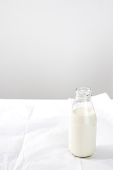 An open bottle of milk is on white crumpled craft paper on the table against the background