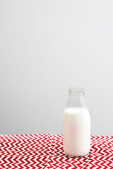An open bottle of milk is on a red and white tablecloth in a zigzag on the table against the background of a gray wall in the kitchen
