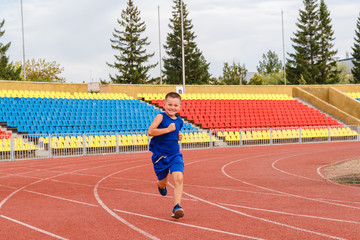 Fototapeta premium Six-year-old boy in sports uniform runs through sports stadium in summer