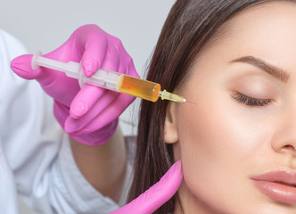 Cosmetologist does prp therapy anti wrinkle and aging skin on the face of a beautiful woman in a...