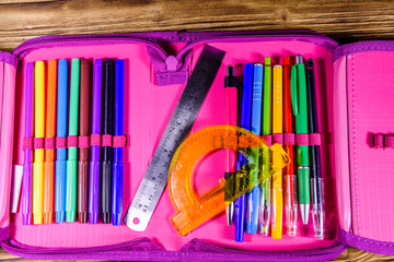 Different school stationeries (pens, pencils, felt tip pens, ruler and protractor) in a pink pencil...