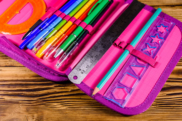 Different school stationeries (pens, pencils, ruler and protractor) in a pink pencil box