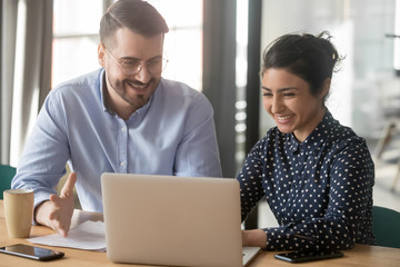 Cheerful hindu woman caucasian man multi-ethnic colleagues working together sit at desk look at...