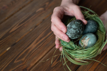 Man holding painted eggs for easter. nest of grass. brown wooden table