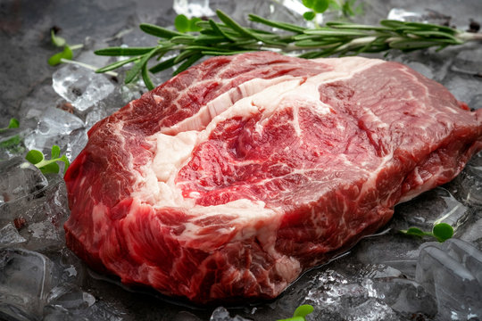 Raw fresh rib eye beef steak on ice with herbs and rosemary