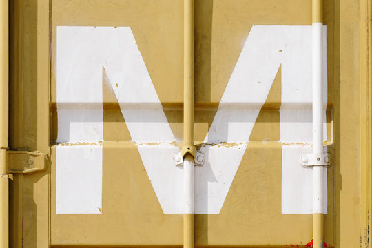 White silk-screen printing of letter M on a yellow shipping container