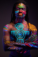 portrait of african man painted in fluorescent paint on face and muscular torso, studio shot with UV light. ethnic prints
