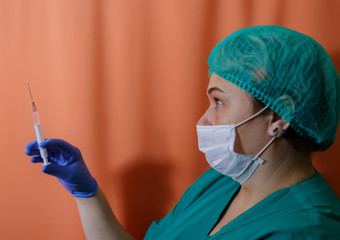 A female doctor in a sterile mask and uniform prepares to give an injection at the time of the...