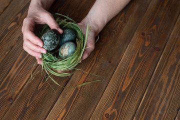 Person holding painted eggs for easter. nest of grass. brown wooden table