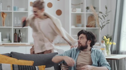 Excited woman snatching smartphone out of hands of her husband and running off. Childish couple smiling and fighting for gadget while having fun during self-isolation at home