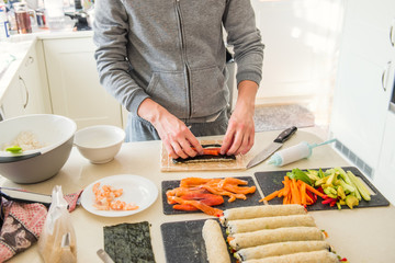 Caucasian man preparing homemade sushi rolls. Filling sushi. The steps for creating sushi with salmon. Process of sushi making by following cooking online video classes via smartphone. Selective focus