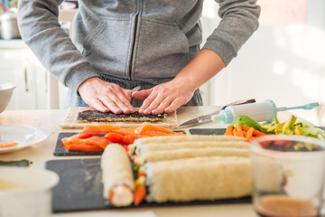 Caucasian man preparing homemade sushi rolls. Forming sushi. The steps for creating sushi with salmon. Process of sushi making by following cooking online video classes via smartphone. Selective focus