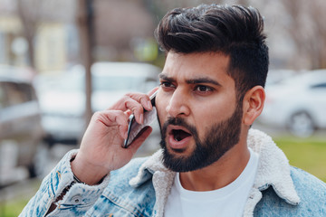 Bearded stylish indian man outdoors using app in his smartphone.